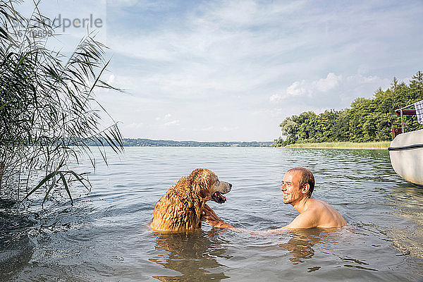 Junger Mann mit seinem Golden Retriever in einem See