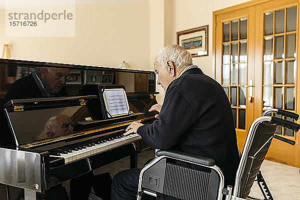 Älterer Mann sitzt im Rollstuhl und spielt zu Hause Klavier