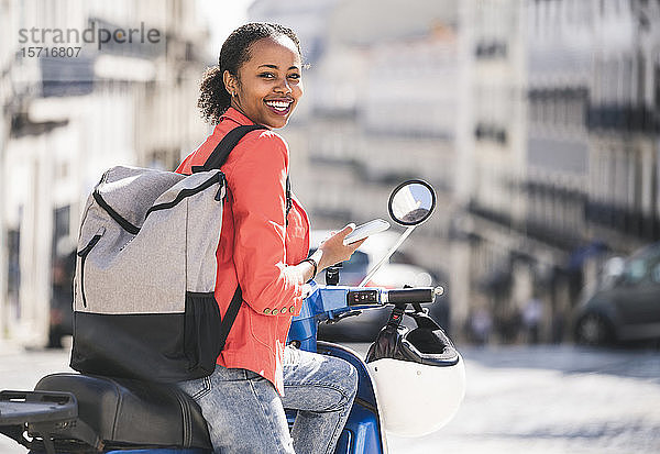 Porträt einer glücklichen jungen Frau mit Motorroller und Handy in der Stadt  Lissabon  Portugal