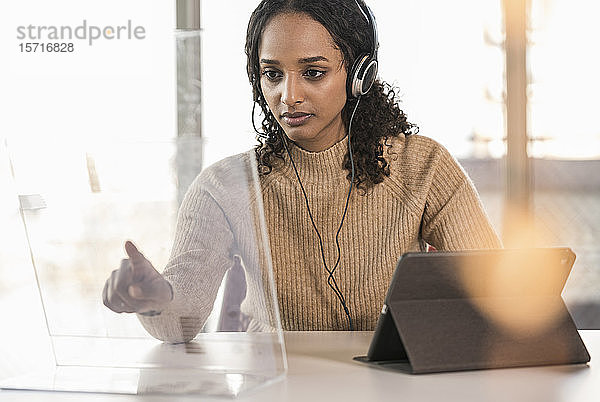 Junge Geschäftsfrau sitzt am Schreibtisch im Büro und benutzt einen transparenten Bildschirm
