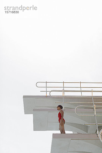 Junge Frau im roten Badeanzug auf dem Highboard stehend