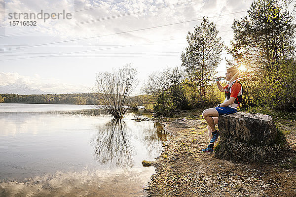 Sportlicher Mann sitzt bei Sonnenuntergang auf einem Felsen am Seeufer  Forstsee  Kärnten  Österreich