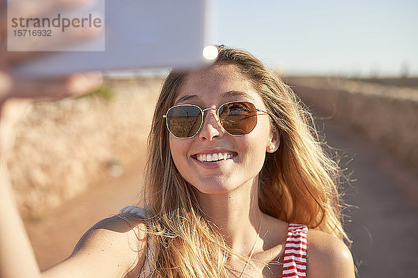 Lächelnde Frau mit Sonnenbrille  die bei Sonnenuntergang Selfie nimmt