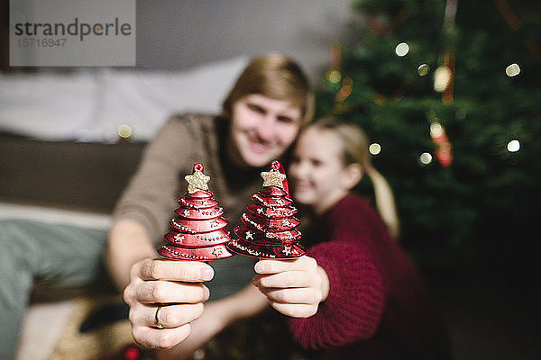 Vater und Tochter zeigen roten Weihnachtsschmuck