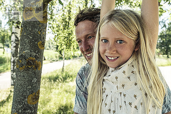 Porträt eines lächelnden Mädchens mit Vater am Ast einer Birke hängend