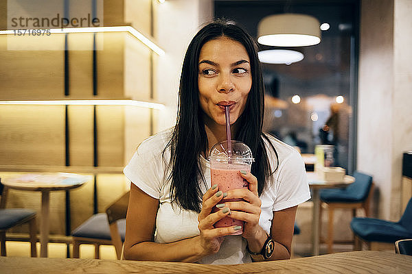 Schwarzhaarige Frau trinkt einen Smoothie im Café