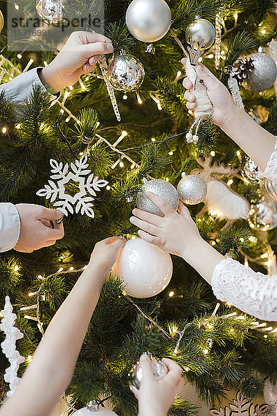Schnittansicht von Kinderhänden beim Schmücken des Weihnachtsbaums