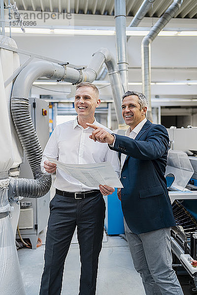 Zwei glückliche Geschäftsleute mit Papier im Gespräch in einer Fabrik