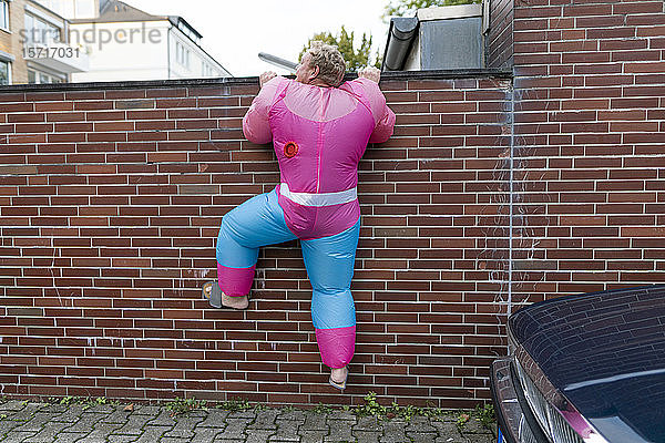Mann in rosa Bodybuilder-Kostüm klettert über eine Wand