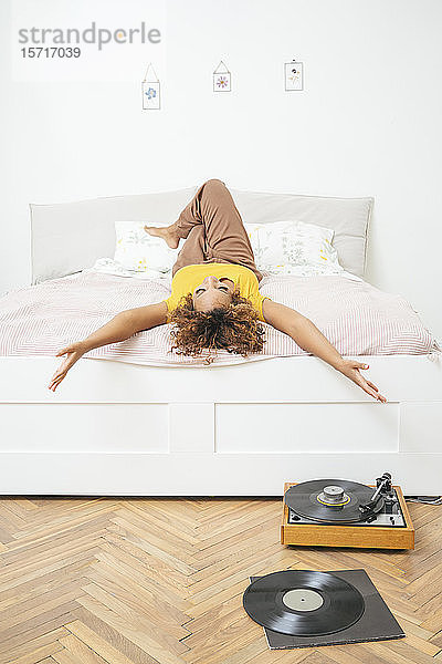Junge Frau liegt zu Hause im Bett mit Plattenspieler auf dem Boden