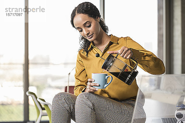 Junge Geschäftsfrau sitzt im Büro am Schreibtisch und macht eine Kaffeepause