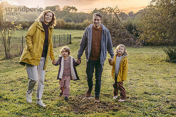 Porträt einer glücklichen Familie mit zwei Töchtern  die im Herbst auf einer Wiese spazieren gehen
