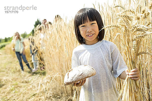 Kleines asiatisches Mädchen steht auf dem Feld  hält Brot und Weizenähren