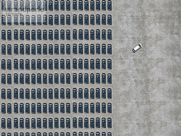 Luftaufnahme eines weißen Autos  das einen mit schwarzen Autos gefüllten Parkplatz verlässt
