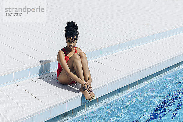 Nachdenkliche junge Frau im roten Badeanzug sitzt am Pool