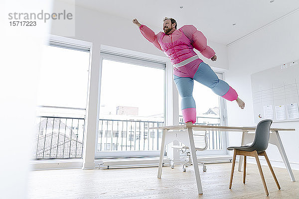 Geschäftsmann im Büro in rosa Bodybuilder-Kostüm  der vorgibt zu fliegen