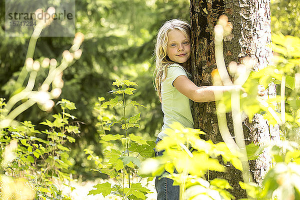 Kleines Mädchen umarmt Baum im Wald