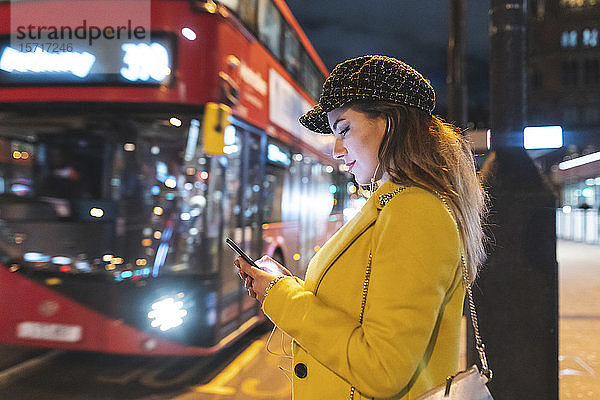Glückliche Frau wartet nachts in der Stadt auf den Bus  London  Großbritannien