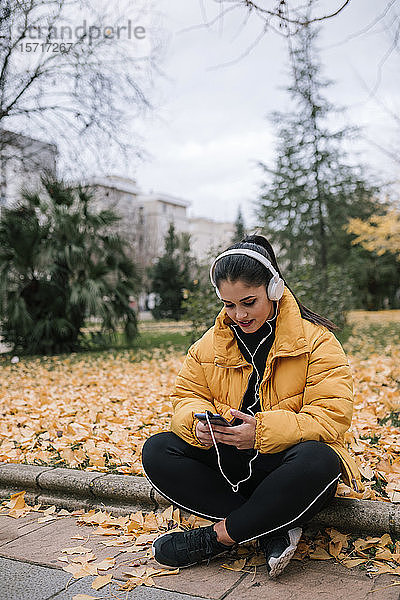 Junge Frau  die im Herbst mit Kopfhörer und Smartphone Musik hört