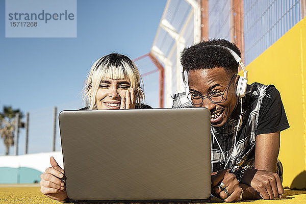 Porträt eines jungen Paares  das sich mit Kopfhörer und Laptop im Freien vergnügt
