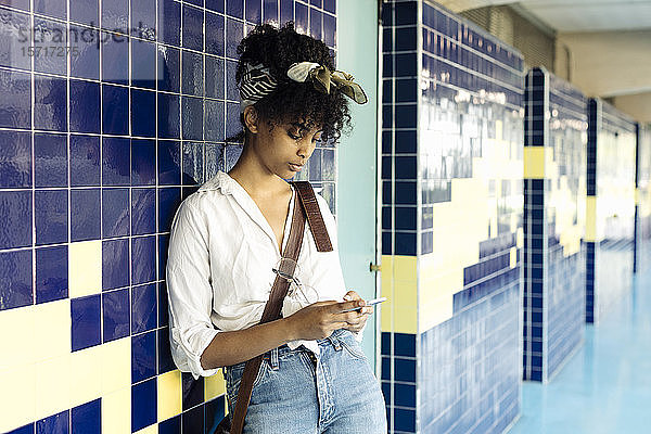 Porträt einer jungen Frau mit lockigem schwarzem Haar  die sich an eine gekachelte Wand lehnt Textnachrichten
