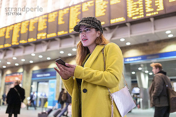 Frau am Bahnhof überprüft ihr Smartphone