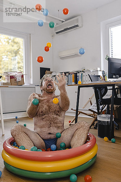 Verrückter Geschäftsmann sitzt im Büro im Planschbecken und spielt mit Bällen