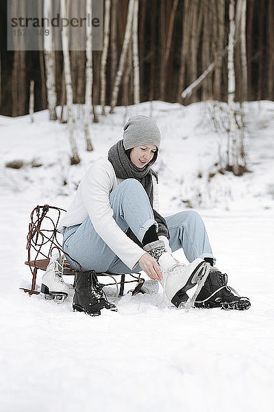 Frau zieht Schlittschuhe auf Schneefeld an