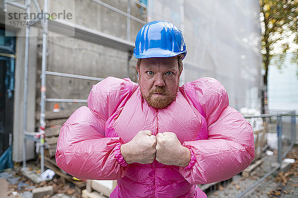 Porträt eines Mannes mit rosa Bodybuilder-Kostüm und Schutzhelm auf einer Baustelle