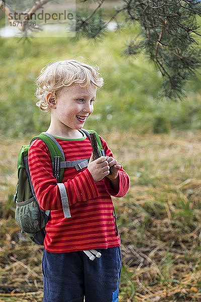 Porträt eines lächelnden blonden Jungen mit Rucksack in der Natur