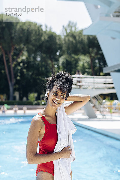 Porträt einer lächelnden jungen Frau in rotem Badetuch vor einem Pool