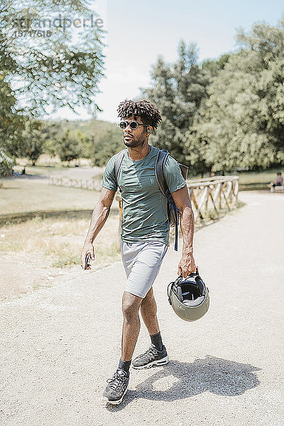 Junger Mann mit Helm geht im Park spazieren