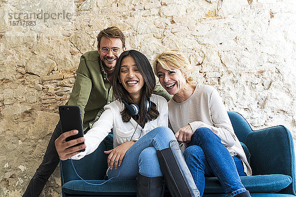 Drei lachende Kollegen in einem Studio  die sich mit einem Smartphone selbstständig machen
