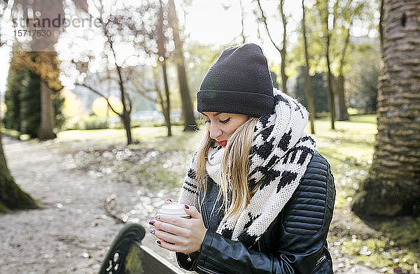 Schöne blonde Frau beim Kaffeetrinken zum Mitnehmen in einem Park