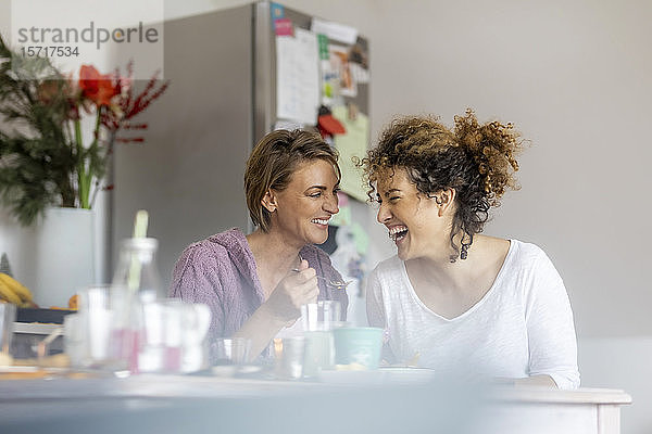Zwei glückliche Frauen sitzen und unterhalten sich zu Hause am Küchentisch