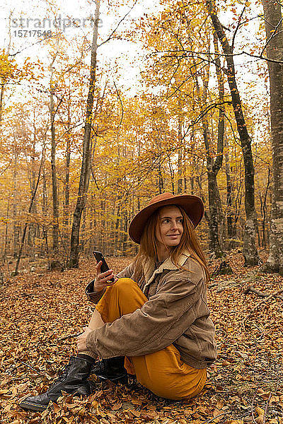 Porträt einer modischen rothaarigen jungen Frau mit Zellphänomen  die im herbstlichen Wald um