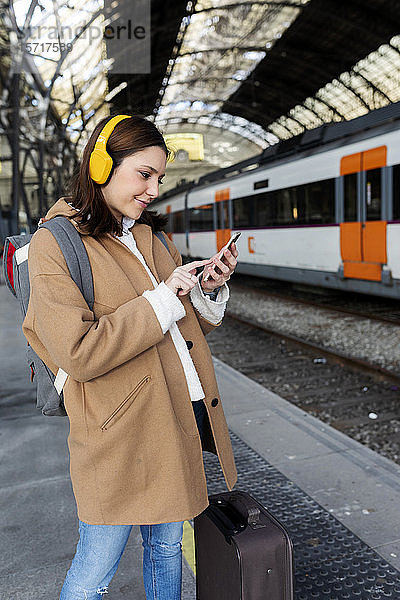 Junge Frau mit Kopfhörern und Handy am Bahnhof