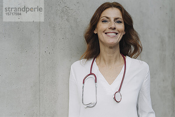 Porträt einer lächelnden Ärztin an einer Betonwand