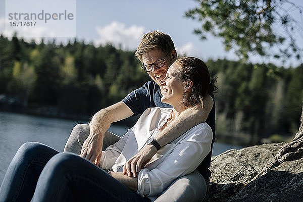 Glückliches Paar sitzt auf einem Felsen am Seeufer  Forstsee  Kärnten  Österreich