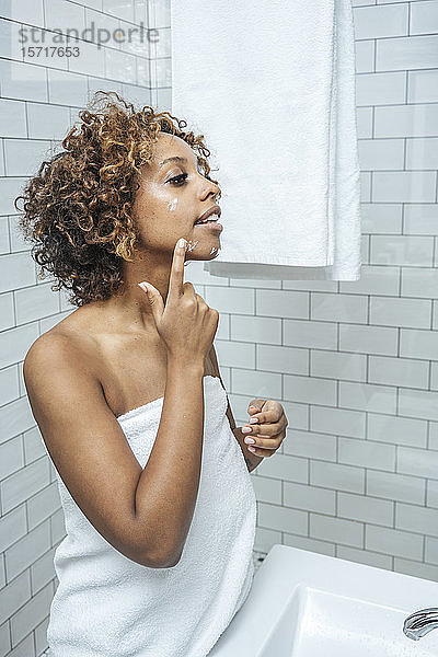Junge Frau im Badezimmer trägt Gesichtscreme auf