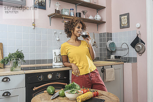 Lächelnde junge Frau trinkt ein Glas Rotwein in der Küche