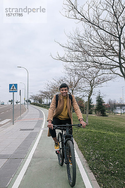Porträt eines lächelnden jungen Mannes beim Fahrradfahren in der Stadt