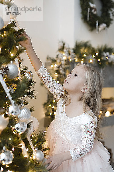 Porträt eines blonden kleinen Mädchens beim Schmücken des Weihnachtsbaums