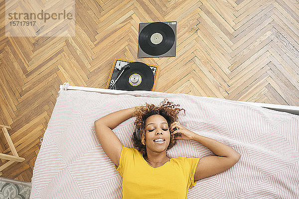 Junge Frau liegt auf dem Bett und hört Musik mit Kopfhörern und Plattenspieler