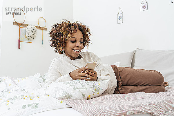 Junge Frau liegt im Bett und benutzt ein Smartphone