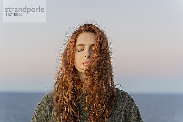 Rothaarige junge Frau mit geschlossenen Augen bei Sonnenuntergang an der Küste  Ibiza  Spanien