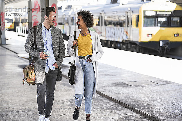 Glücklicher junger Geschäftsmann und Geschäftsfrau  die am Bahnhof spazieren gehen und sich unterhalten