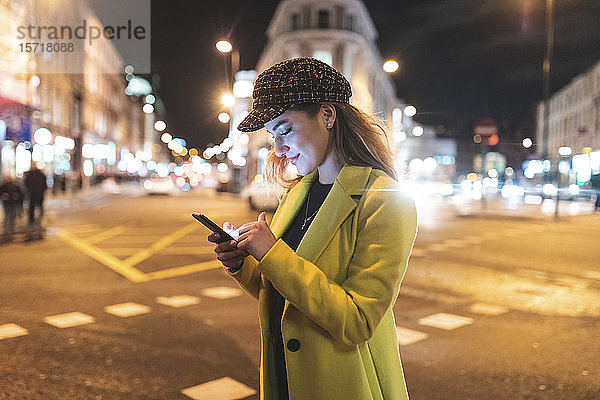 Frau mit ihrem Smartphone in der Stadt nachts neben einer Straße