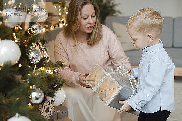 Mutter gibt ihrem kleinen Sohn ein Geschenk in der Nähe des Weihnachtsbaums