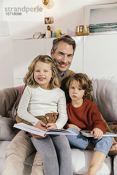 Porträt eines glücklichen Vaters beim Buchlesen mit Töchtern auf der Couch